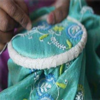 A Chikankari artisan meticulously hand-stitching delicate floral patterns on fabric, creating intricate embroidery.